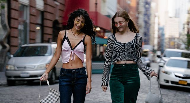 Two stylish women walking in a vibrant city street, showcasing fashion trends.