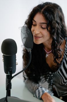 Young woman recording podcast using a professional microphone indoors. Perfect for tech and lifestyle themes.
