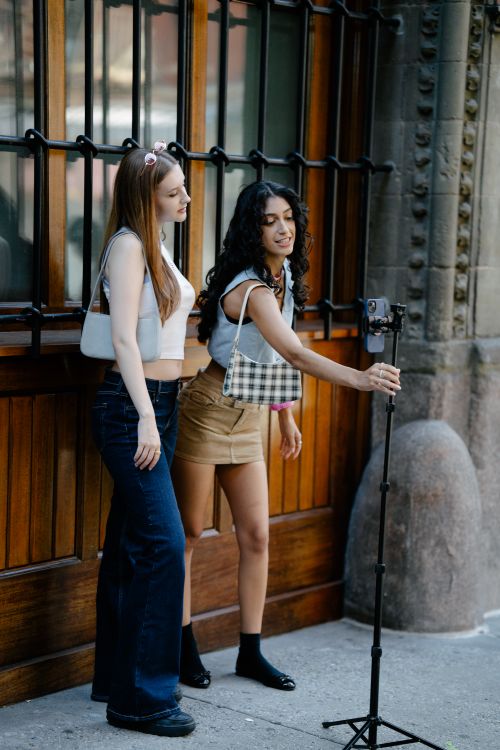 Free Two young women using a smartphone on a tripod outdoors, capturing content. Stock Photo