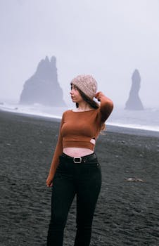 Stylish woman on Iceland's famous Reynisfjara black sand beach with towering rock formations in the background.