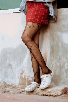Fashionable woman in plaid skirt and fishnet stockings standing stylishly against a wall in Lagos.