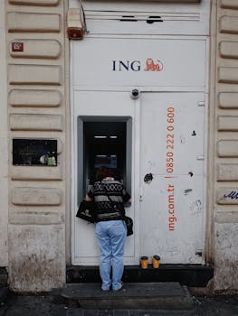 Back view of a person using an ING bank ATM on a city street.