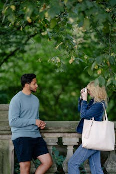 A man and woman engaging in a casual photo session in a lush park setting.