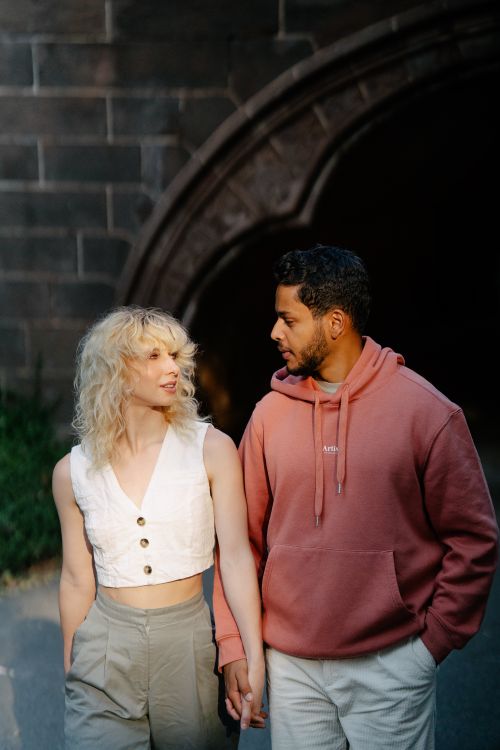 Free A couple holding hands and talking while walking in an outdoor urban area. Stock Photo