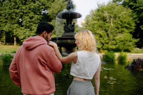 Free A couple shares a tender moment by a fountain in a lush park setting. Stock Photo