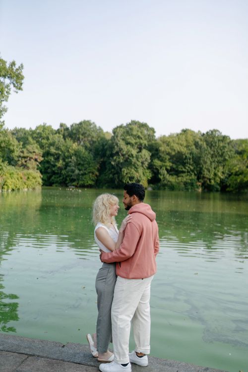 Free Couple embracing near a calm lake with lush greenery, capturing a serene and loving moment. Stock Photo
