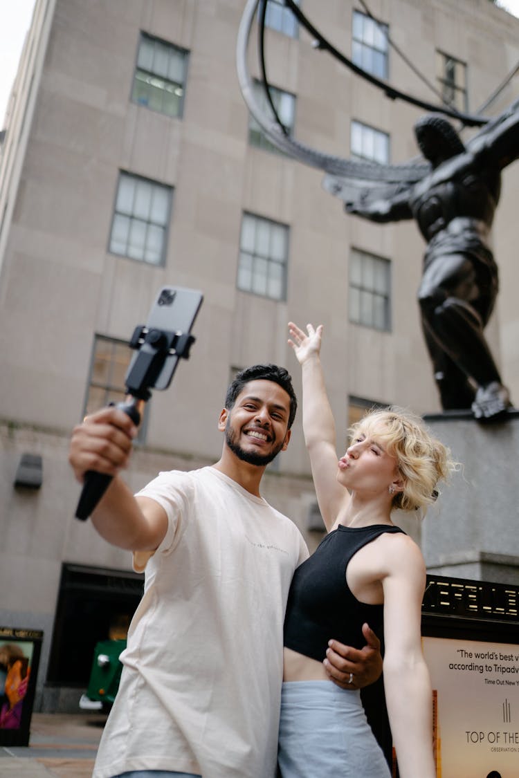 Brunette Man And Blond Woman Taking A Selfie Under A Metal Statue