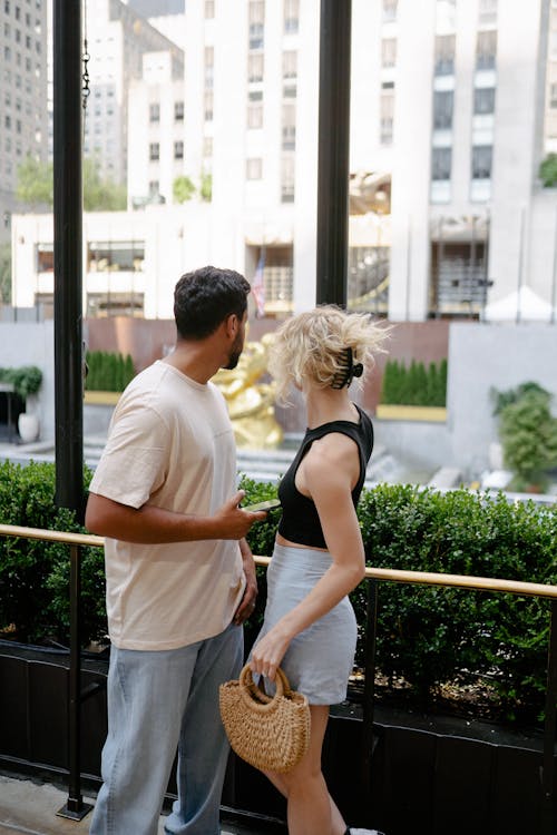 Free Man with a Woman Holding a Straw Handbag Looking at City Buildings Stock Photo