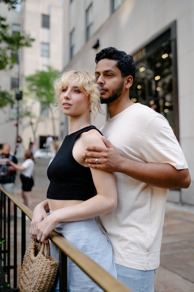 Brunette Man Standing Behind And Embracing Blonde Woman On A City Street