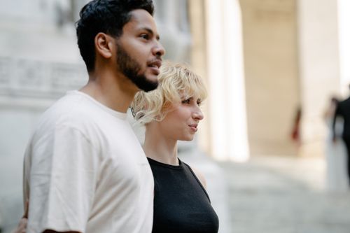 Free A diverse couple walking together, exploring an urban architectural setting with bright natural lighting. Stock Photo