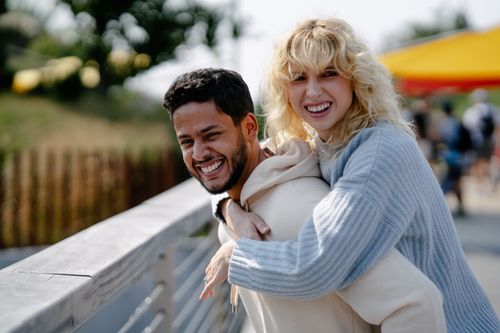 Free A joyful couple sharing a loving piggyback moment outdoors on a sunny day. Stock Photo