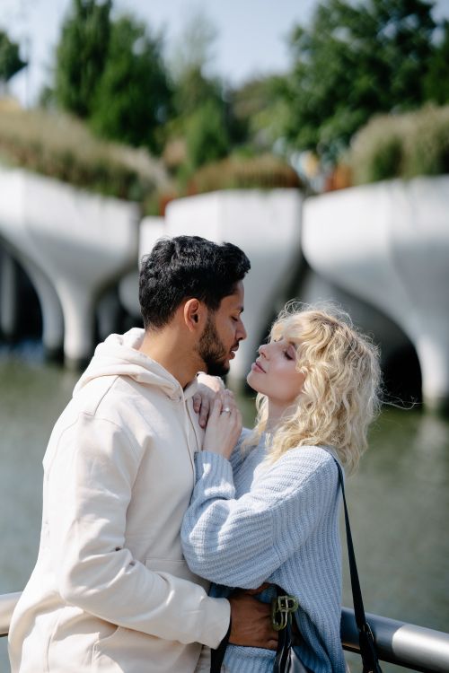 Free A loving couple embraces by a serene lakeside in a sunny outdoor park setting. Stock Photo