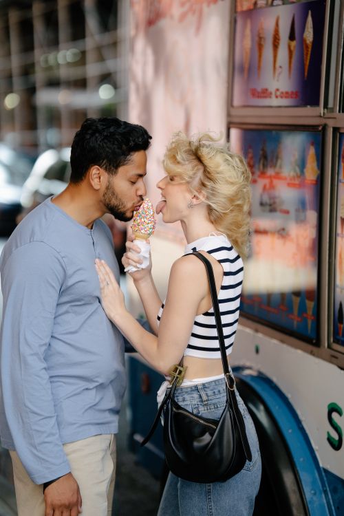 Free A couple enjoys a playful moment sharing an ice cream cone by an ice cream van. Stock Photo