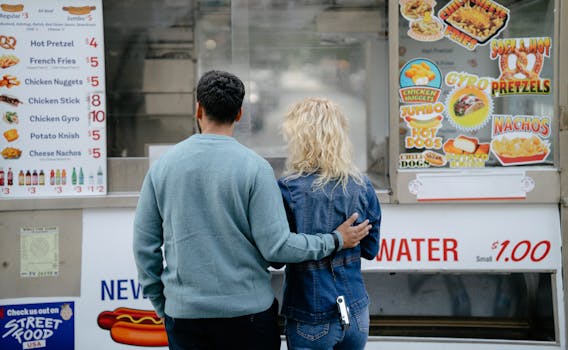 Back view of a couple selecting snacks at an urban food truck, featuring various fast food options.