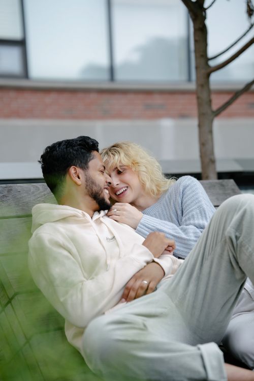 Free Happy couple sitting on a bench outdoors, sharing a tender moment with smiles and warmth. Stock Photo