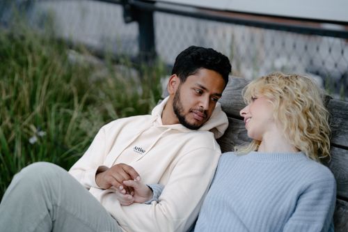 Free A couple sitting closely and holding hands, enjoying a relaxing moment together outdoors. Stock Photo