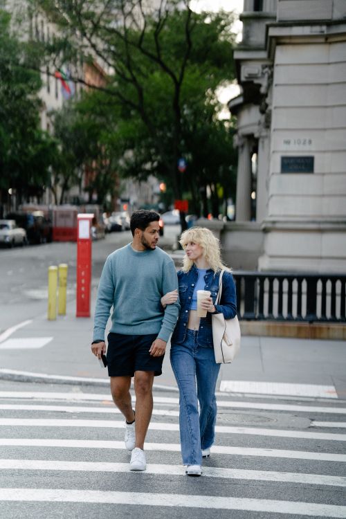Free A young couple walking across a city street, surrounded by classic architecture. Stock Photo