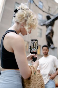 A young woman records a man in an urban setting using a smartphone.
