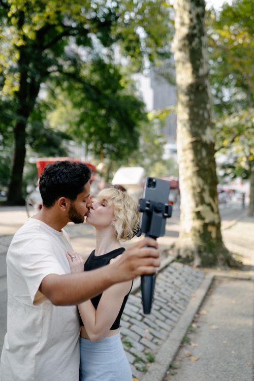 Free A romantic couple takes a selfie while kissing in a sunny outdoor setting, capturing an intimate moment. Stock Photo