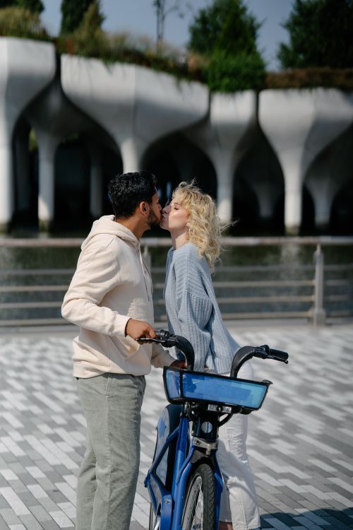 Free A couple sharing a tender kiss by a bicycle in an outdoor urban setting with stunning architecture. Stock Photo