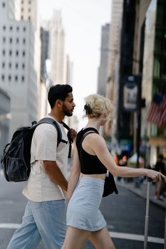 Young couple with backpacks walking through a city street enjoying a sunny day.