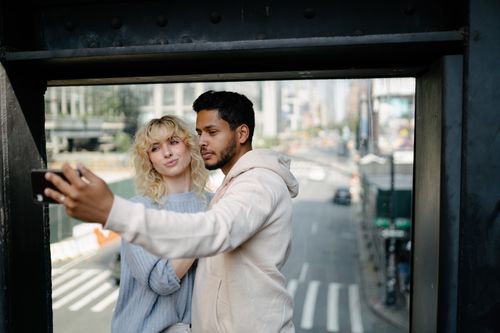 Free A young couple taking a selfie on a bridge overlooking a city street. Stock Photo