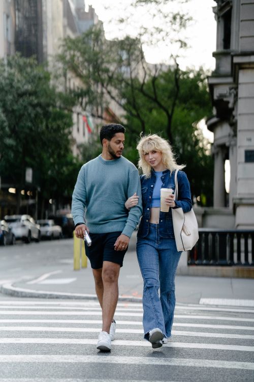 Free A happy couple walks arm-in-arm across a city street, enjoying a casual stroll on a sunny day. Stock Photo