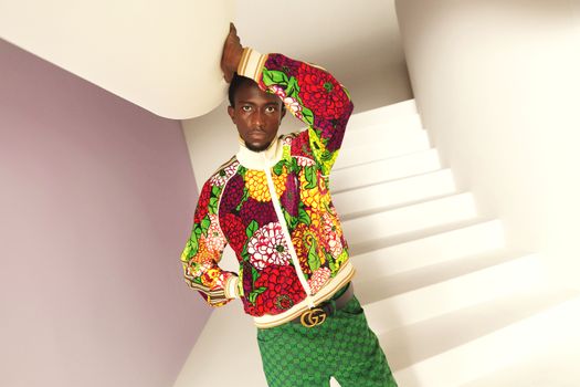 Portrait of a man in vibrant floral fashion posing on a staircase indoor setting.