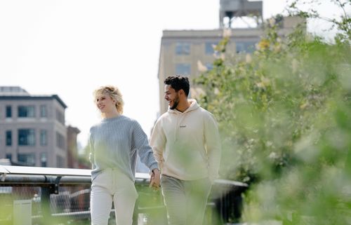 Free A smiling couple holds hands while walking in an urban park with greenery around. Stock Photo