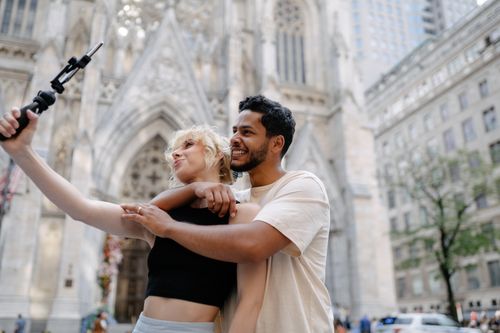 Free Happy couple taking a selfie in front of a historic cathedral, embracing and smiling. Stock Photo