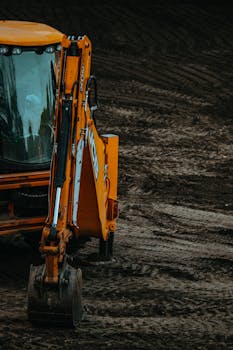 Close-up of a yellow excavator on a construction site with muddy terrain.