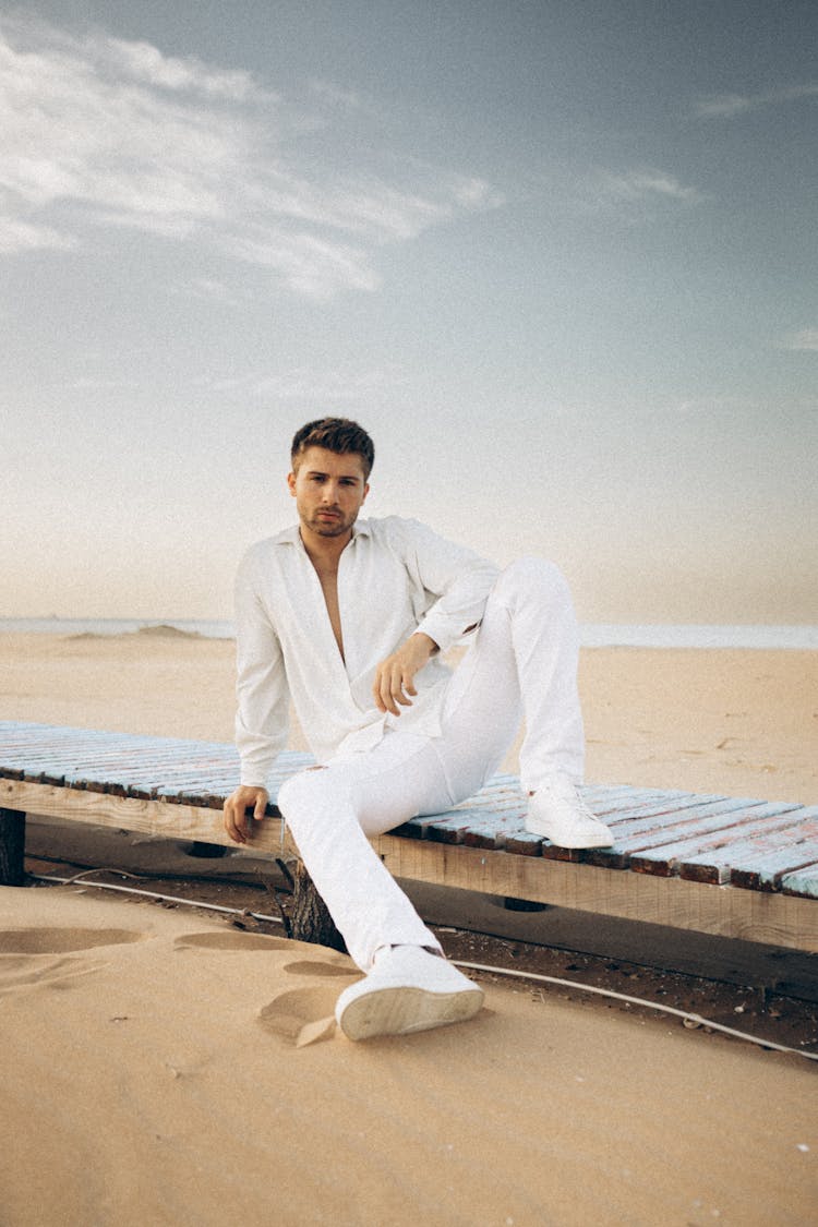 Young Man In A White Outfit Sitting On The Beach 