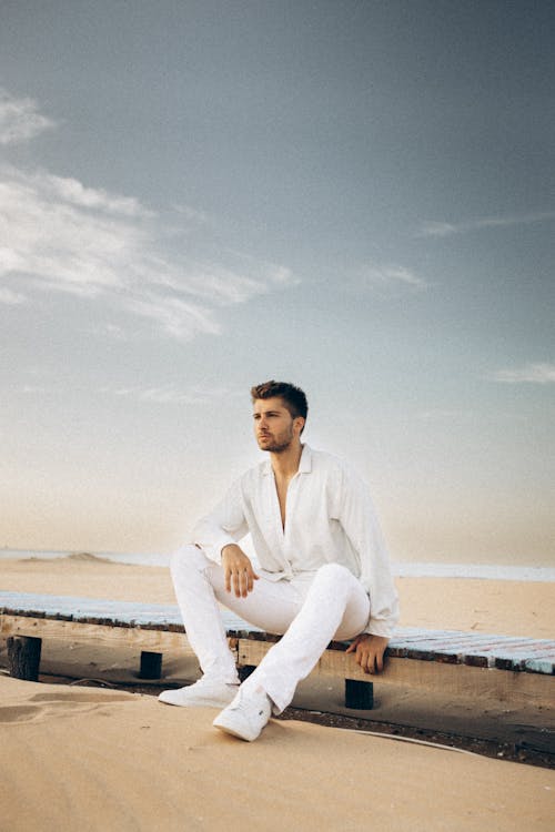 A Man in White Long Sleeves Sitting on Wooden Dock while Looking Afar
