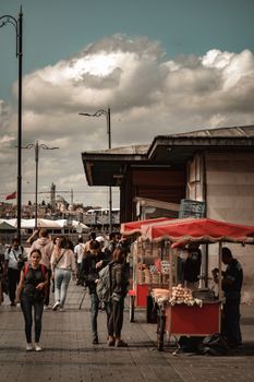 Vibrant urban scene with people walking by busy street food stalls under cloudy sky.