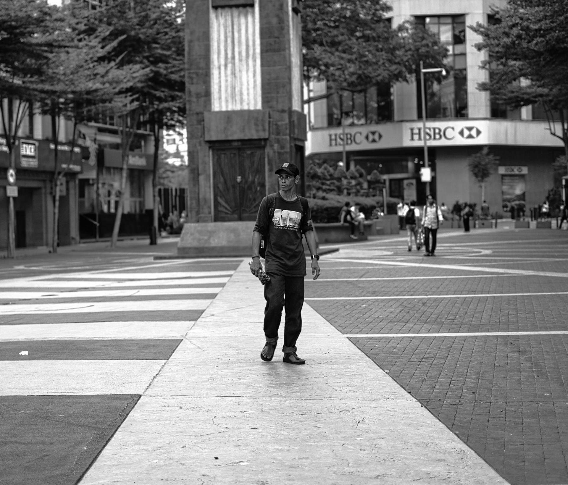 Monochrome view of a man walking in an urban city with a distinctive building in the background.