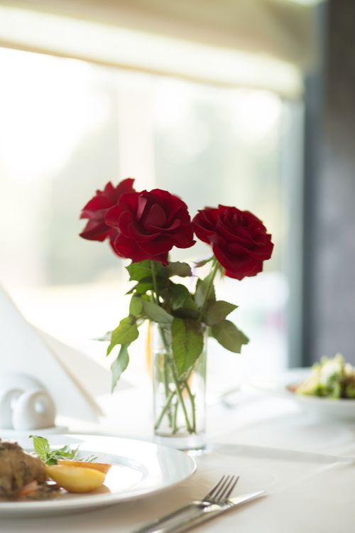 Free A beautifully set table with vibrant red roses in a vase creating a romantic ambiance. Stock Photo