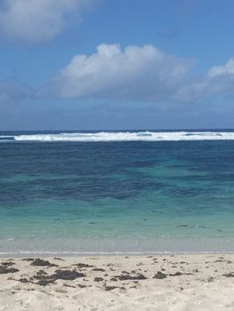 Idyllic beach scene with turquoise waters and gentle waves under a bright sky.