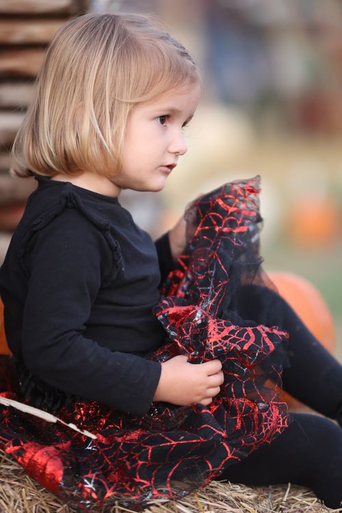 Free A young girl in a Halloween costume sits thoughtfully on a hay bale outdoors. Stock Photo