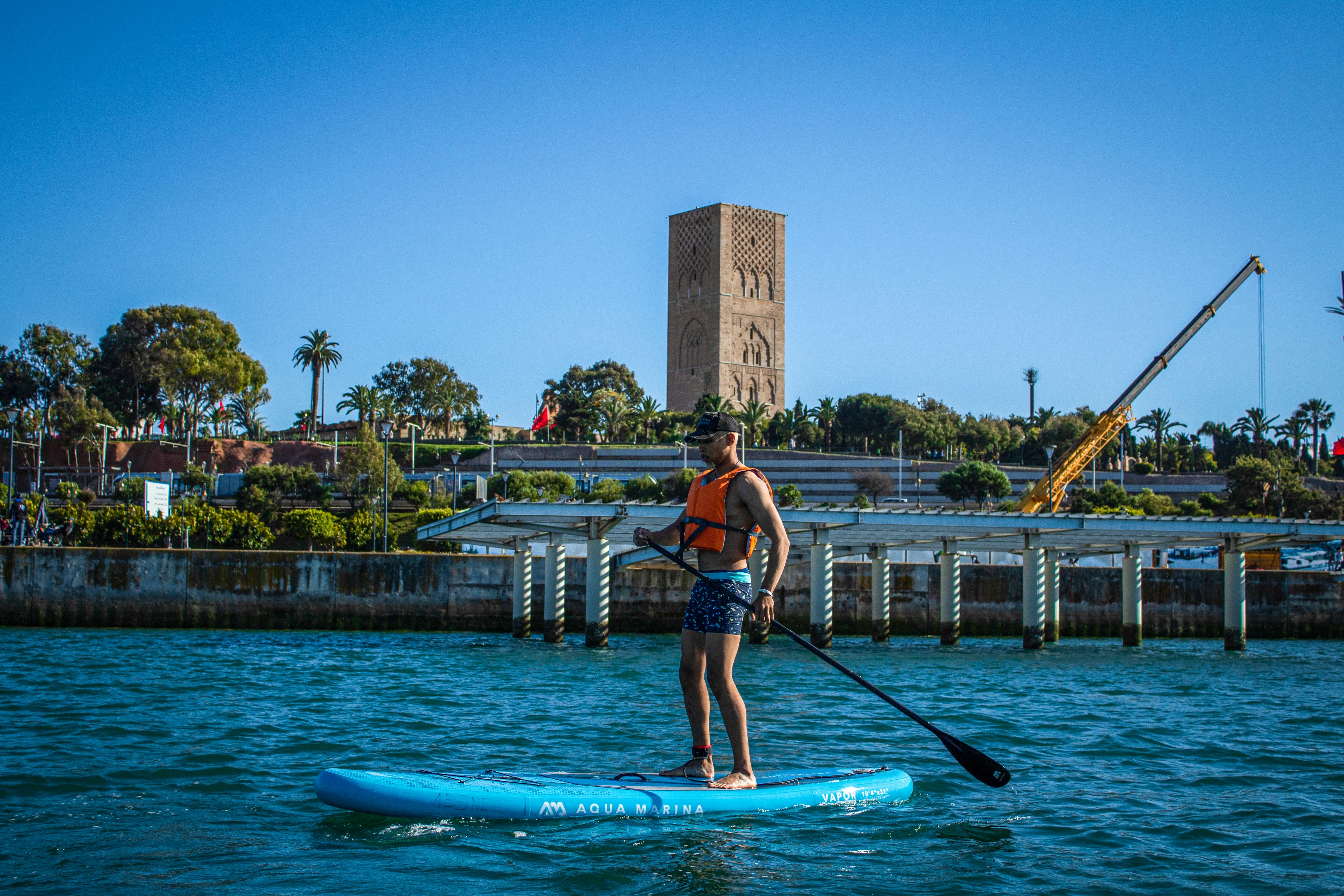 Man enjoying paddle boarding near Hassan Tower in Rabat, showcasing water sports in Morocco.