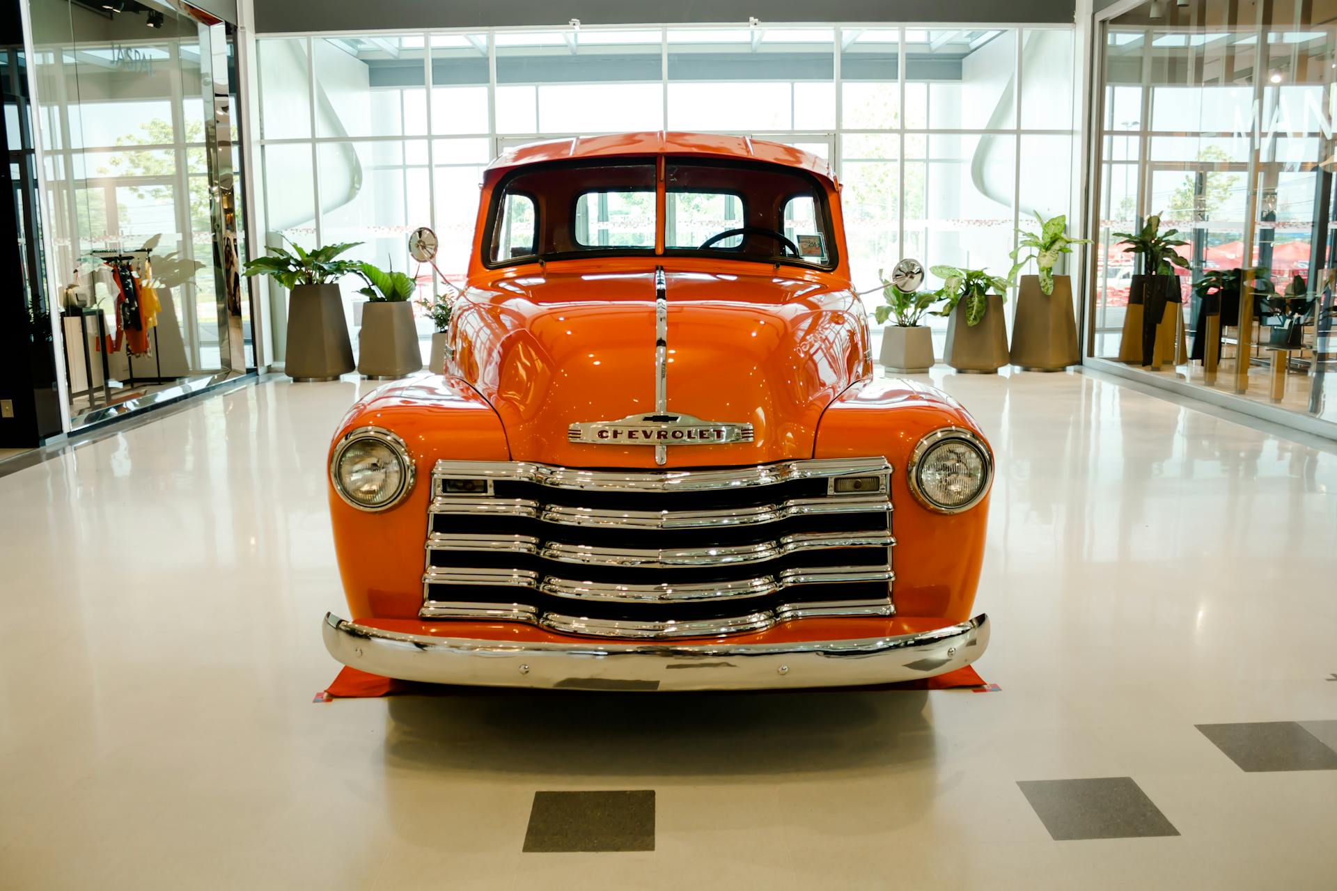 Front view of a vintage orange Chevrolet truck displayed in a modern showroom.