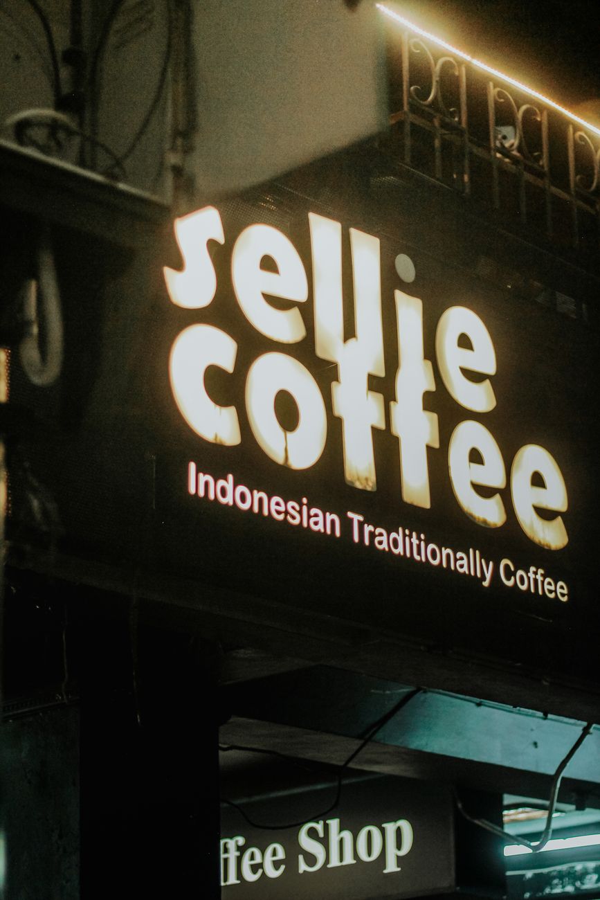 Bright coffee shop signage with Indonesian traditional theme glowing at night.