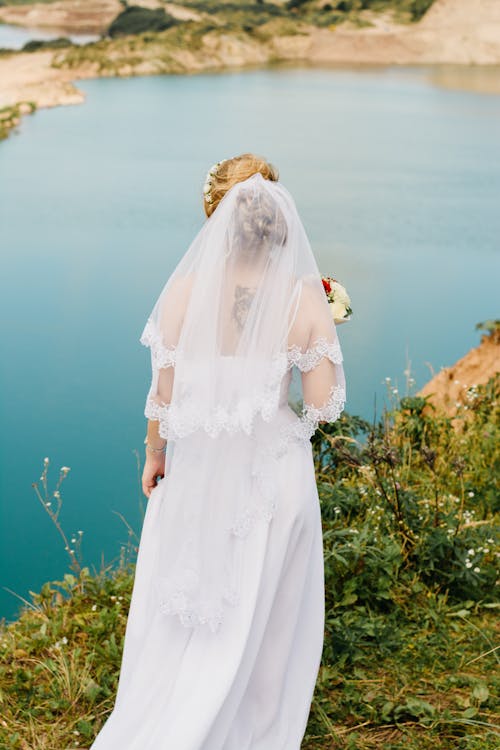 Woman Wearing White Lace Wedding Gown Standing Near the Cliff