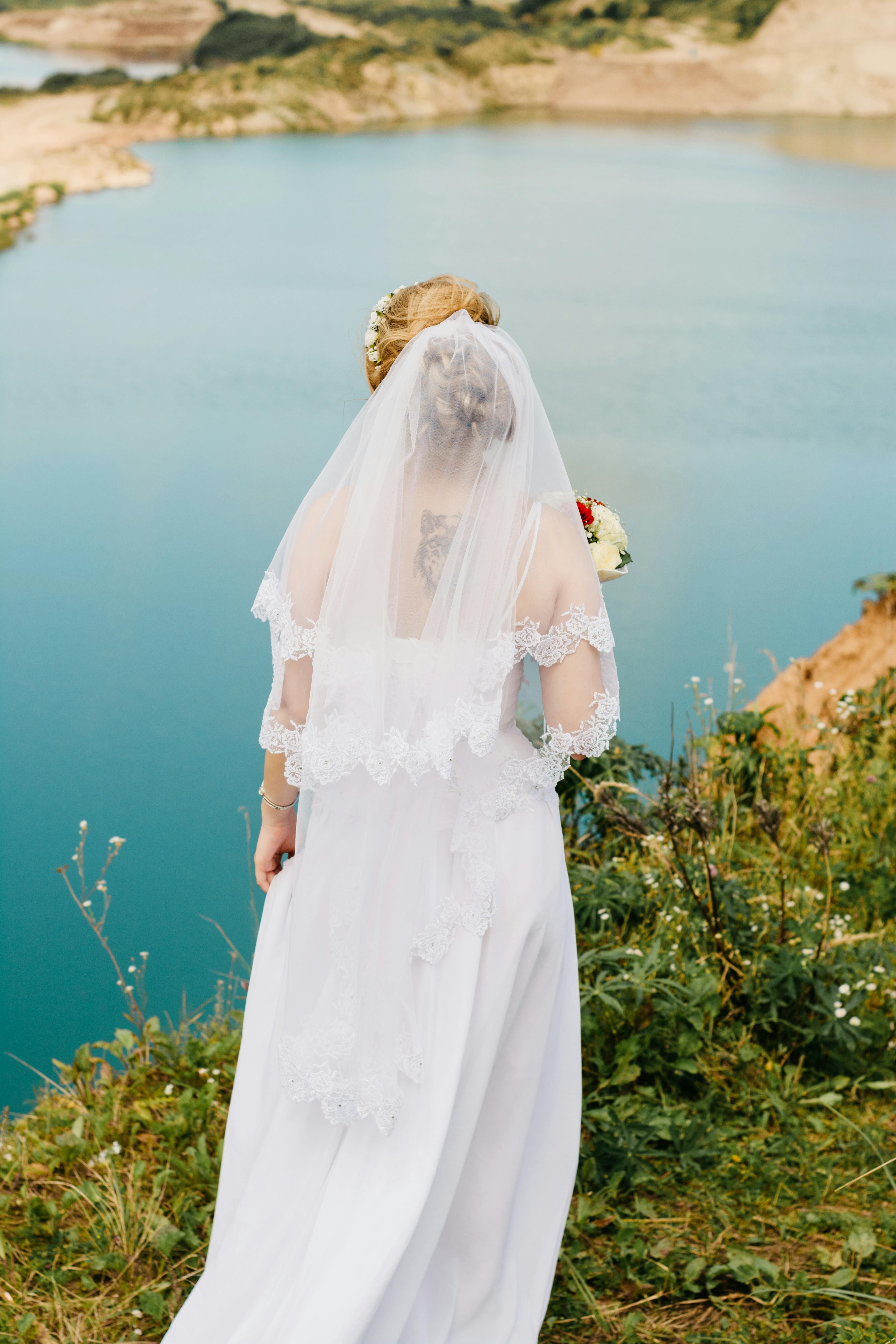 崖の近くに立っている白いレースのウェディングドレスを着ている女性 無料の写真素材