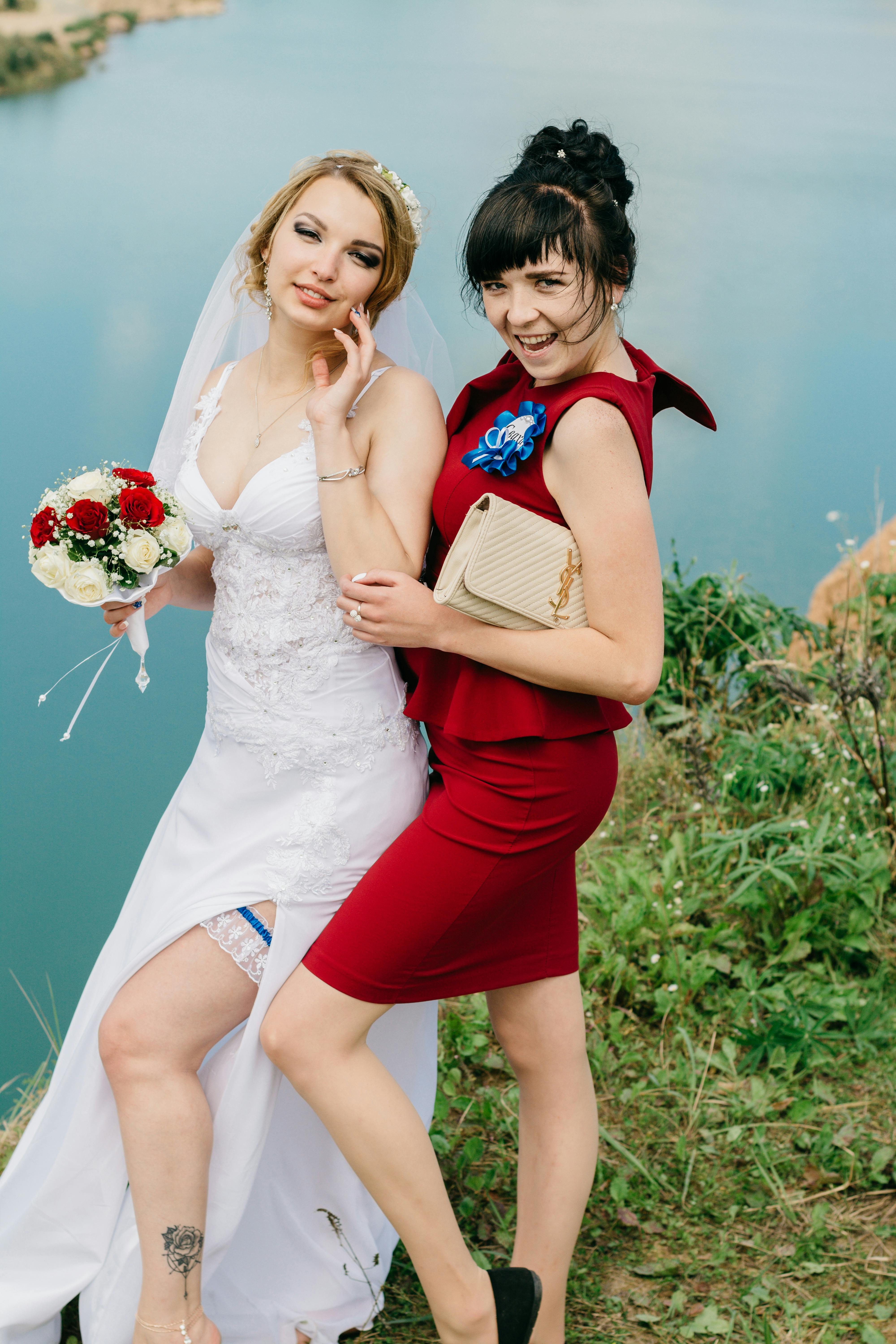 一位微笑的新娘手捧花束，和身着红衣的伴娘一起站在宁静的湖边
