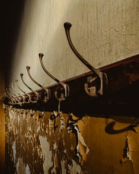 A row of rusty hooks aligned on a wall with peeling paint, casting dramatic shadows.