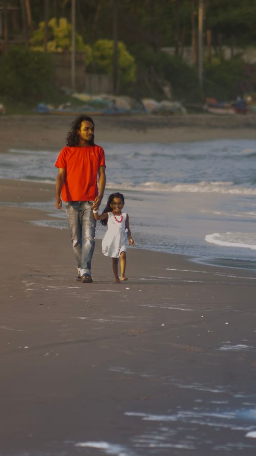 Free Father and daughter enjoy a peaceful walk on a sandy beach during a sunny day. Stock Photo