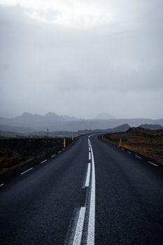 A deserted road stretches into misty mountains under a cloudy sky, ideal for travel-themed content.