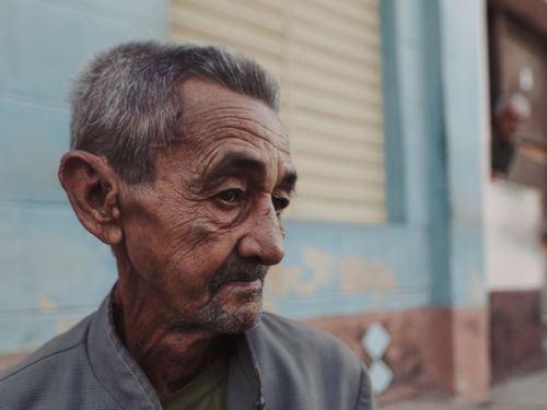 Free Close-up of an elderly man with gray hair standing against a city backdrop. Stock Photo