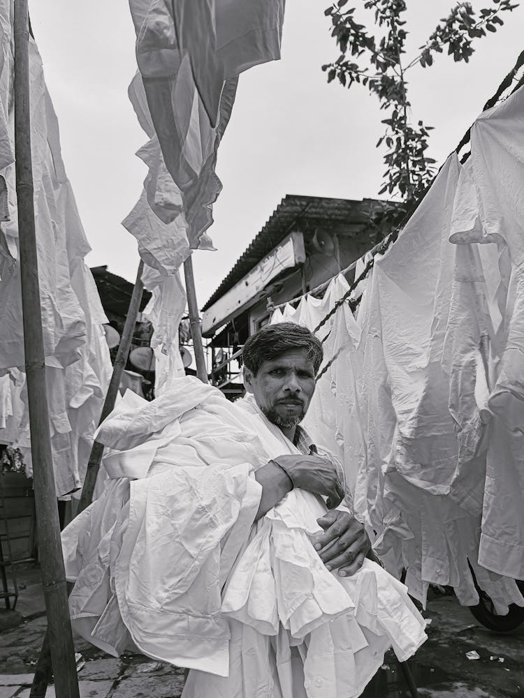 Grayscale Photo Of A Man Carrying A Pile Of White Clothes 