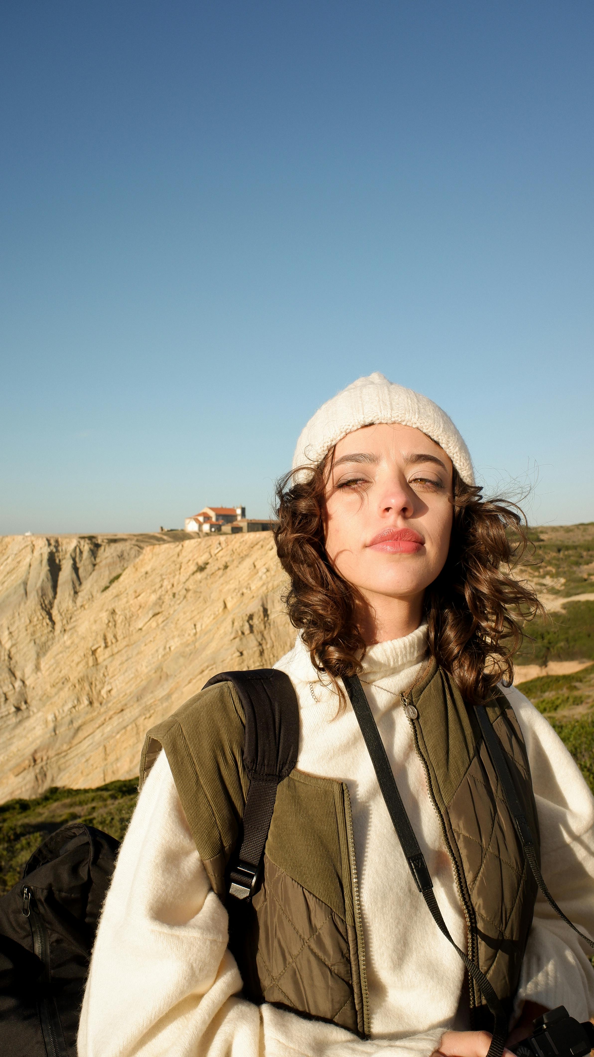 A woman wearing a beanie enjoys a sunny day at a coastal cliffside.